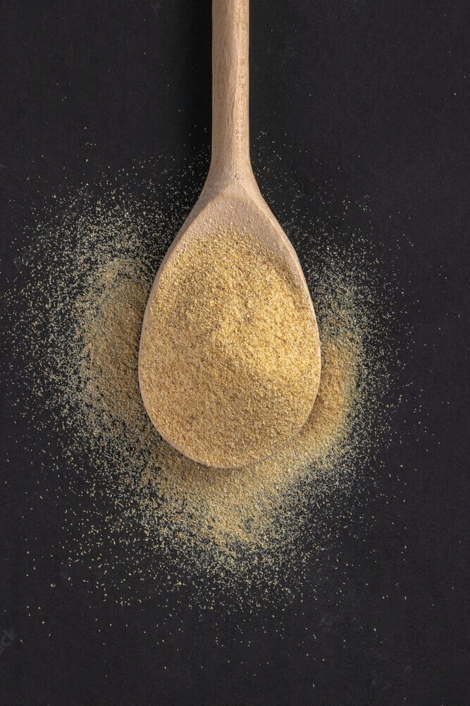 Freshly ground EK Foods garlic powder gracefully placed on a large wooden spoon.