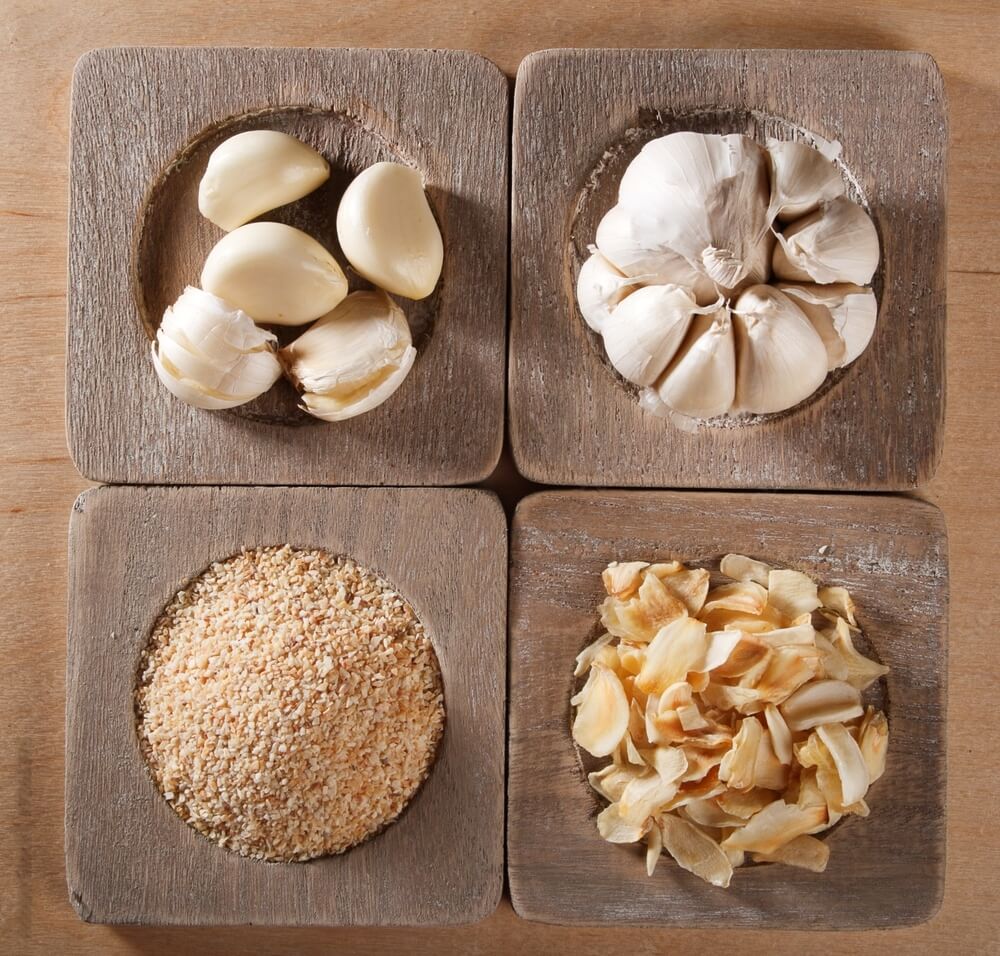 Wooden dish with separate sections for a whole garlic, garlic cloves, dried cloves, and garlic powder.