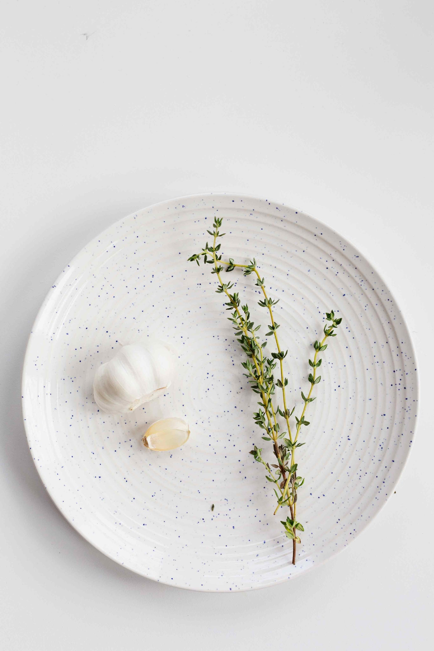 Fresh garlic and thyme neatly arranged on a white plate.