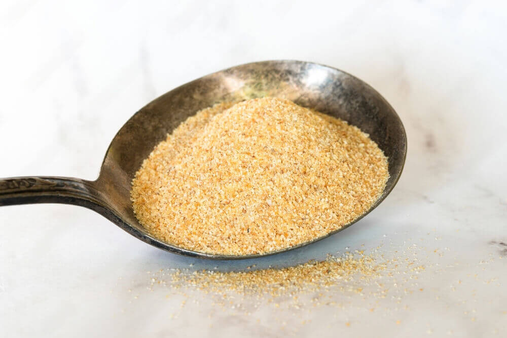 Pure EK Foods garlic powder showcased in a large metallic spoon, highlighting its high quality and versatility.